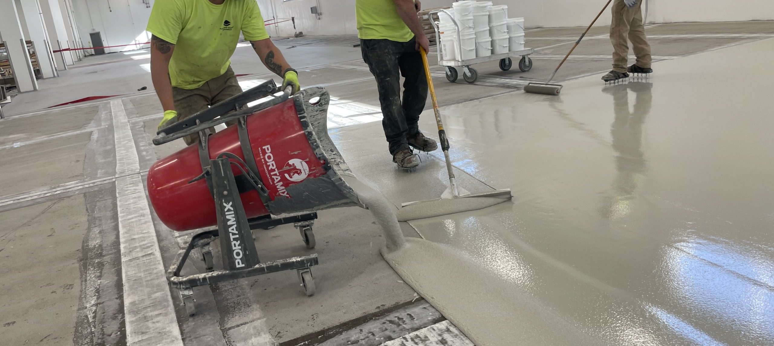 Workers pouring and smoothing freshly mixed concrete on a construction site, using a concrete pump and finishing tools.