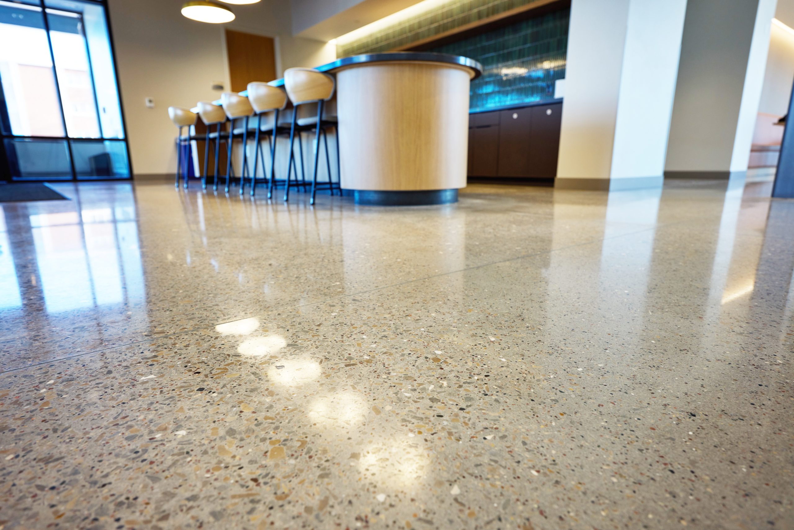 Polished concrete floor in a modern office interior, featuring a sleek bar area with wooden stools and large windows allowing natural light.