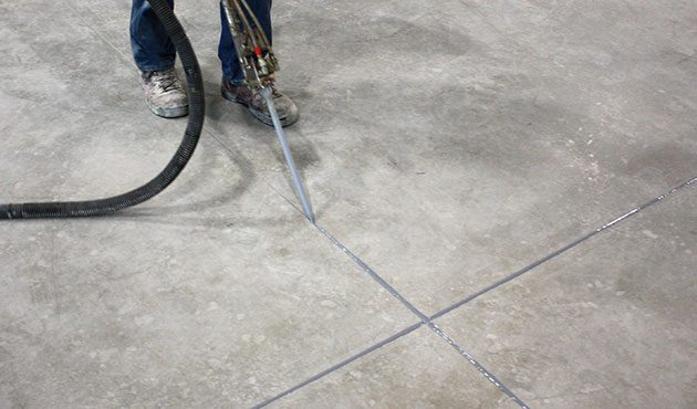 Worker using a caulking gun to apply sealant in the joints of a concrete floor, ensuring durability and preventing moisture infiltration.