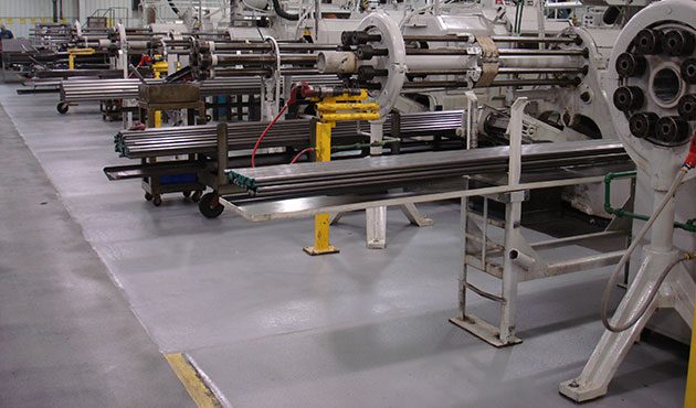 Industrial manufacturing floor with multiple machines and equipment for processing metal rods, featuring organized workstations and a clean, spacious layout.