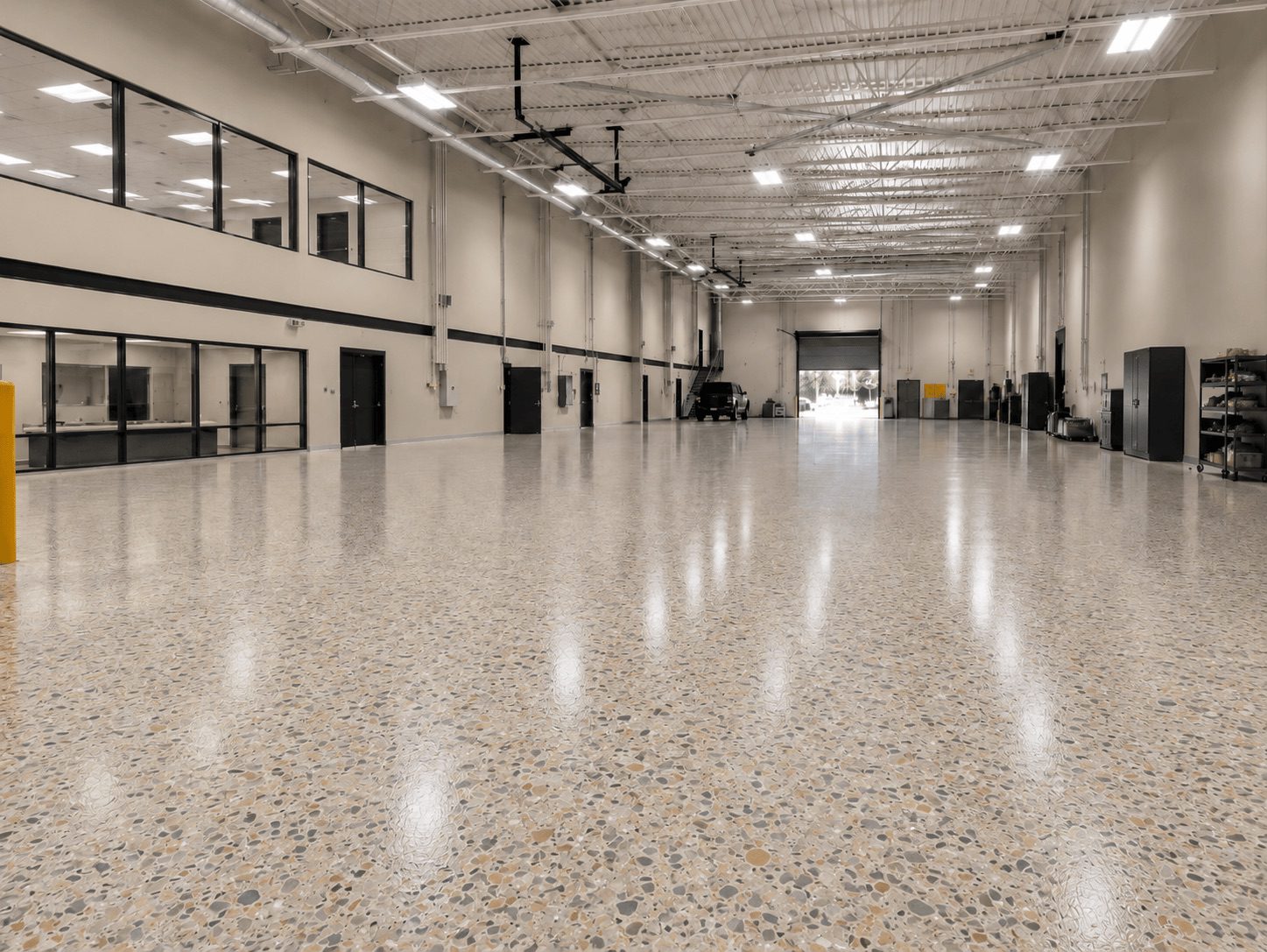 Spacious industrial warehouse interior with polished terrazzo flooring, large windows, and multiple entry points, ideal for storage or manufacturing operations.