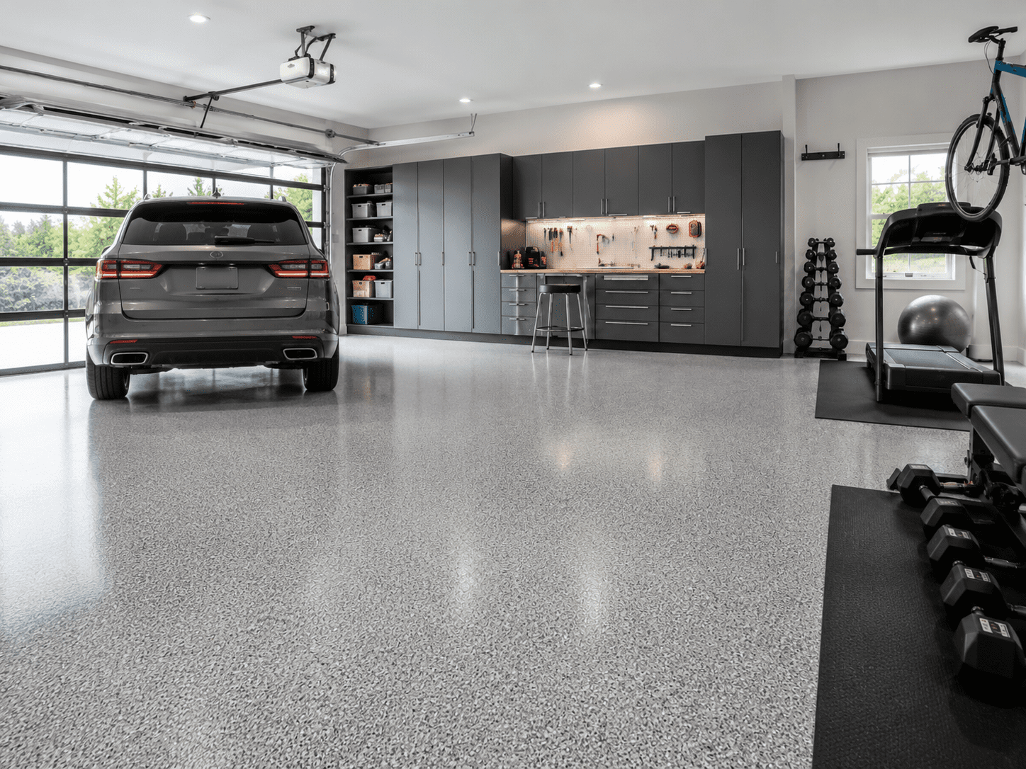 Modern garage interior featuring a sleek gray car, polished epoxy flooring, and contemporary cabinetry, showcasing an organized and stylish space for vehicle storage and home projects.