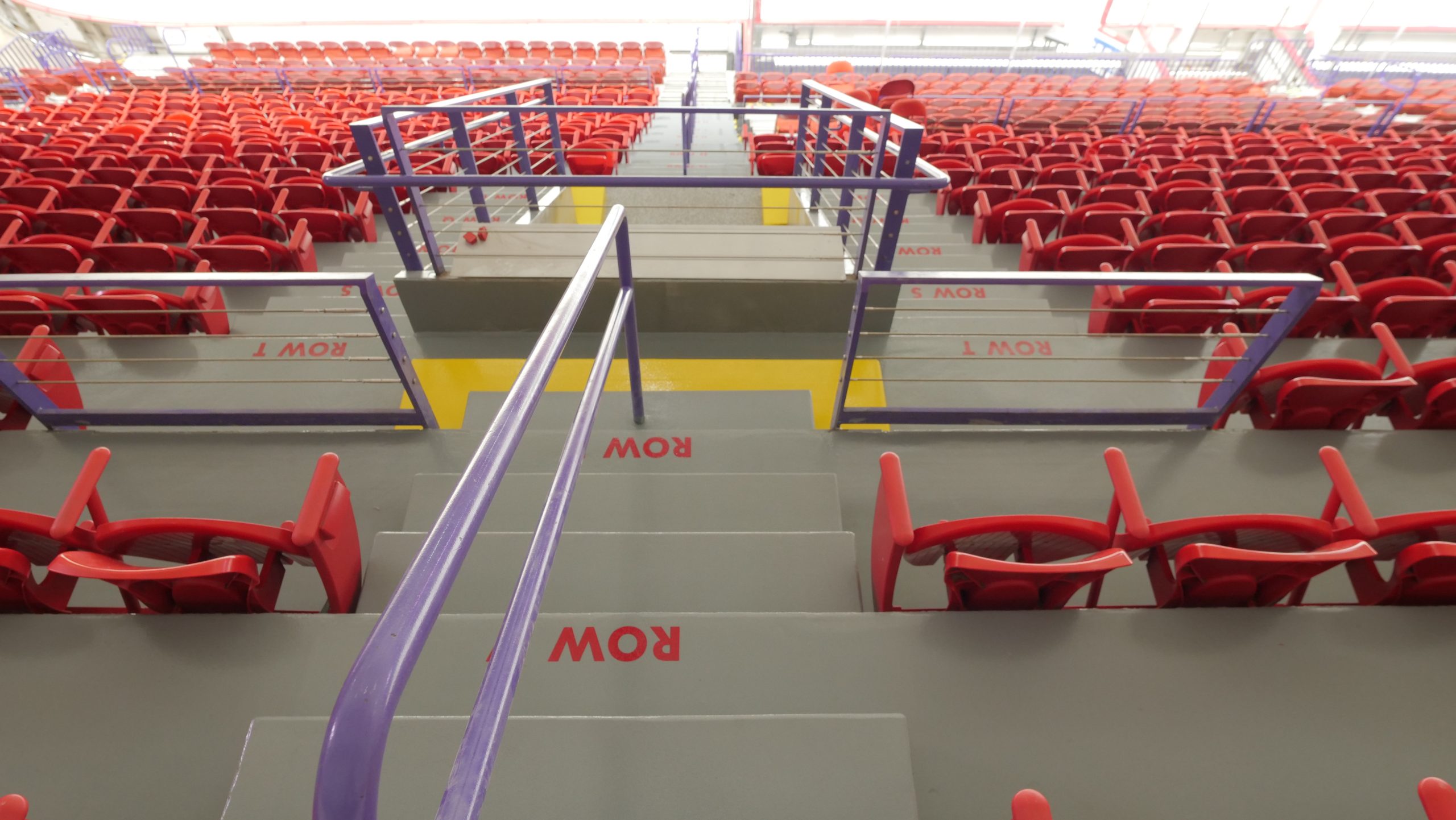 Interior view of a sports arena seating area, showcasing rows of bright red seats and clearly marked steps with row numbers, designed for easy navigation.