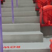 Stadium seating area featuring gray steps with a purple railing and red plastic seats, labeled with row numbers for easy navigation.